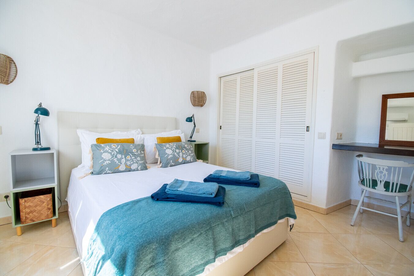 A neatly arranged bedroom with a bed, bedside tables, a desk, and a wardrobe.