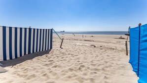 En sandstrand med ett randigt avspärrningsband och en blå presenning.