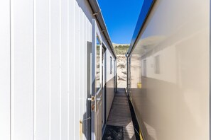 A narrow corridor with a wooden deck leading to a door, surrounded by white walls and a clear blue sky. - Cozy Beachfront Retreat With Scenic Terrace (Koudekerke)