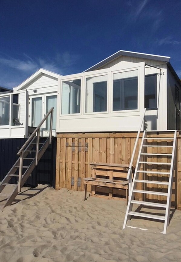 A beach house with a wooden deck, a set of stairs, and a ladder. - Cozy Beachfront Retreat With Scenic Terrace (Koudekerke)