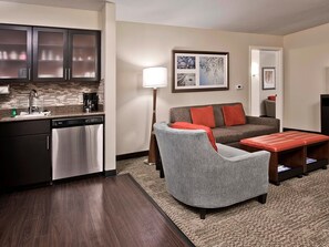 A compact living space with a kitchenette, a grey armchair, a sofa with red cushions, and a floor lamp. - Spacious Ballantyne Suite | Free Breakfast & Pool (Charlotte)