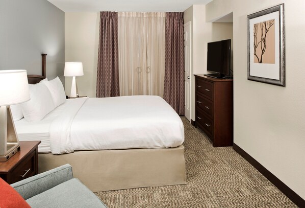 A hotel room with a bed, bedside lamps, a TV, a dresser, and a framed picture on the wall.