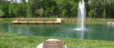 A Kid Pond with a wooden deck, a fountain, and a plaque.