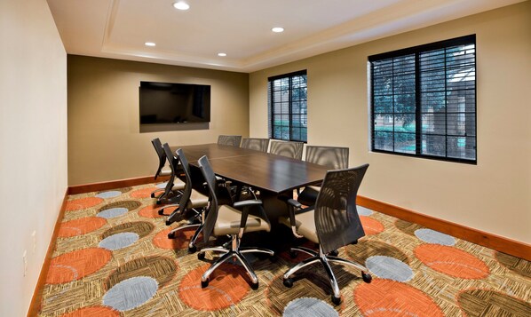 A conference room with a large table, chairs, a flat-screen TV, and windows with blinds.