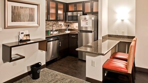 A modern kitchen with dark cabinets, stainless steel appliances, a granite countertop, and a bench. - Accessible Suite in Ballantyne w/ Free Breakfast (Charlotte)