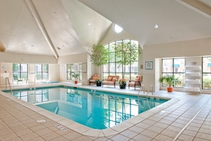 An indoor swimming pool with tiled flooring, lounge chairs, and potted plants.