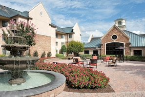 A courtyard with a fountain, outdoor seating, and a building with a clock tower.