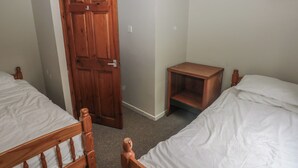 Un dormitorio con dos camas de madera, una mesita de noche de madera, una puerta de madera y una lámpara de pared blanca.