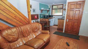 Una sala de estar con un sofá de cuero marrón, una mesa de centro de madera y una cocina al fondo.