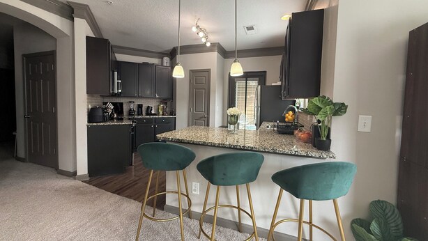 A modern kitchen with dark cabinets, a granite countertop, and three green bar stools. - Velvet Vibes Retreat - A Corporate Work, Play, Stay Getaway (Pooler)