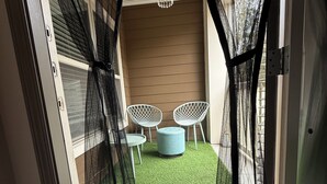 A room with a view through a mesh screen, featuring a small seating area with two chairs and a round ottoman, a hanging light fixture, and a door with a screen. - Velvet Vibes Retreat - A Corporate Work, Play, Stay Getaway (Pooler)