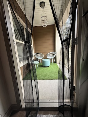 A room with a view through a mesh screen, featuring a small seating area with two chairs and a round ottoman, a hanging light fixture, and a door with a screen. - Velvet Vibes Retreat - A Corporate Work, Play, Stay Getaway (Pooler)
