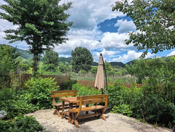 Un conjunto de banco y mesa de madera en un jardín con valla y árboles.