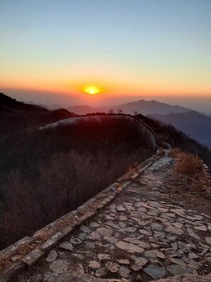 Un sentier de pierres qui monte une colline, avec un coucher de soleil en arrière-plan.