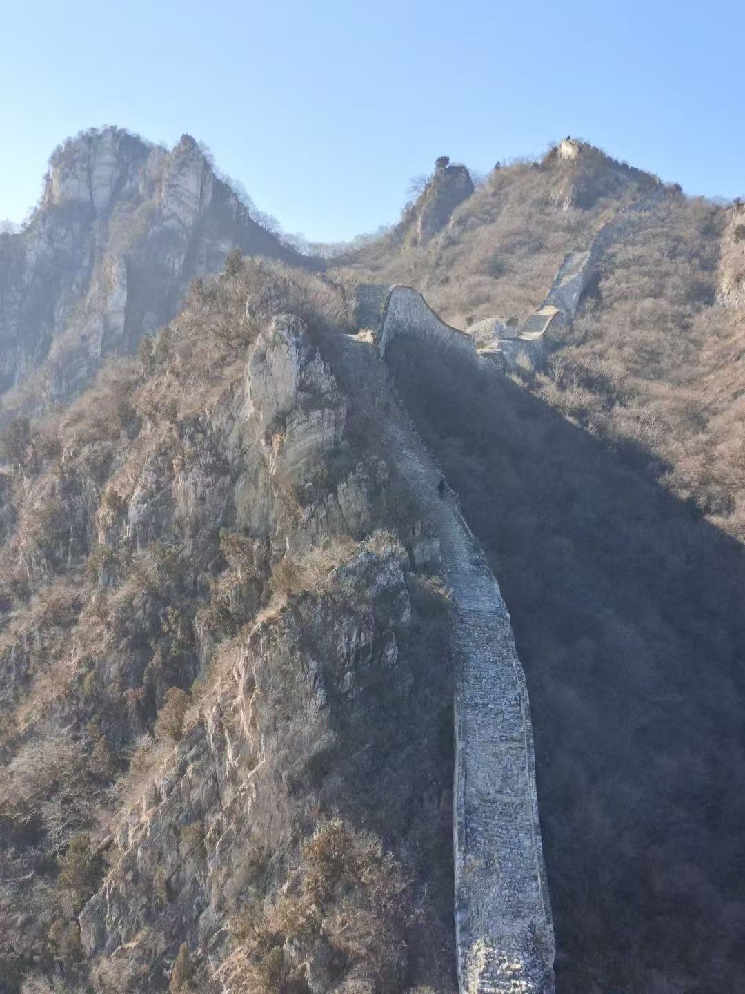 A mountainous landscape with a long, narrow structure, possibly a dam or wall, extending vertically.