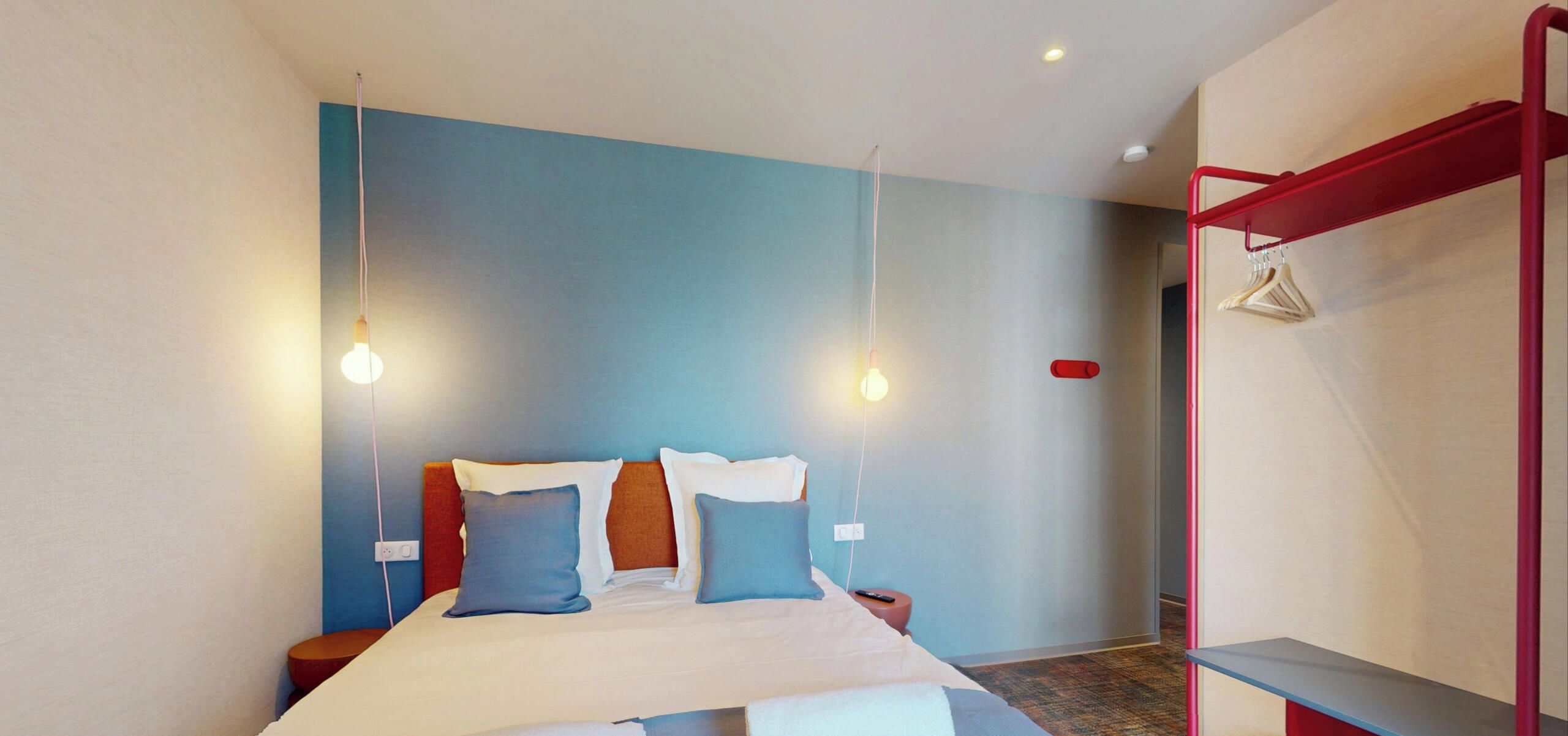 Una habitación de hotel moderna con una cama, mesitas de noche e iluminación colgante.