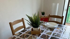 Een eettafel met een tafelkleed met koffieprint, een potplant en een servies met wit serviesbestek.