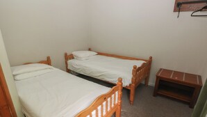 Una habitación pequeña con dos camas de madera, una mesita de madera y una estantería en la pared.