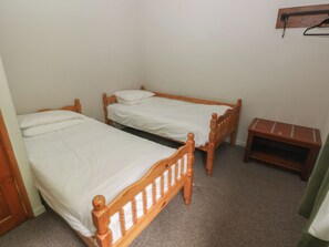 A small room with two wooden beds, a small wooden table, and a wall-mounted shelf. - Cabin No. 13 - Salt and Fern Cabins (Port Talbot)