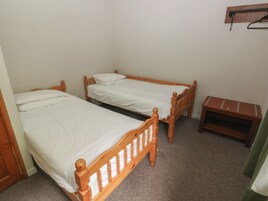 Una habitación pequeña con dos camas de madera, una mesita de madera y una estantería en la pared.