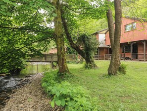 A rustic cabin with a pond, surrounded by lush greenery and a wooden fence. - Cabin No. 13 - Salt and Fern Cabins (Port Talbot)