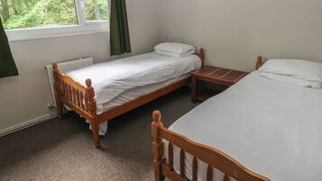 A room with two wooden beds, a window with curtains, and a radiator.