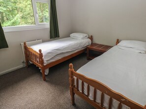 Une chambre avec deux lits en bois, une fenêtre avec des rideaux et un radiateur.