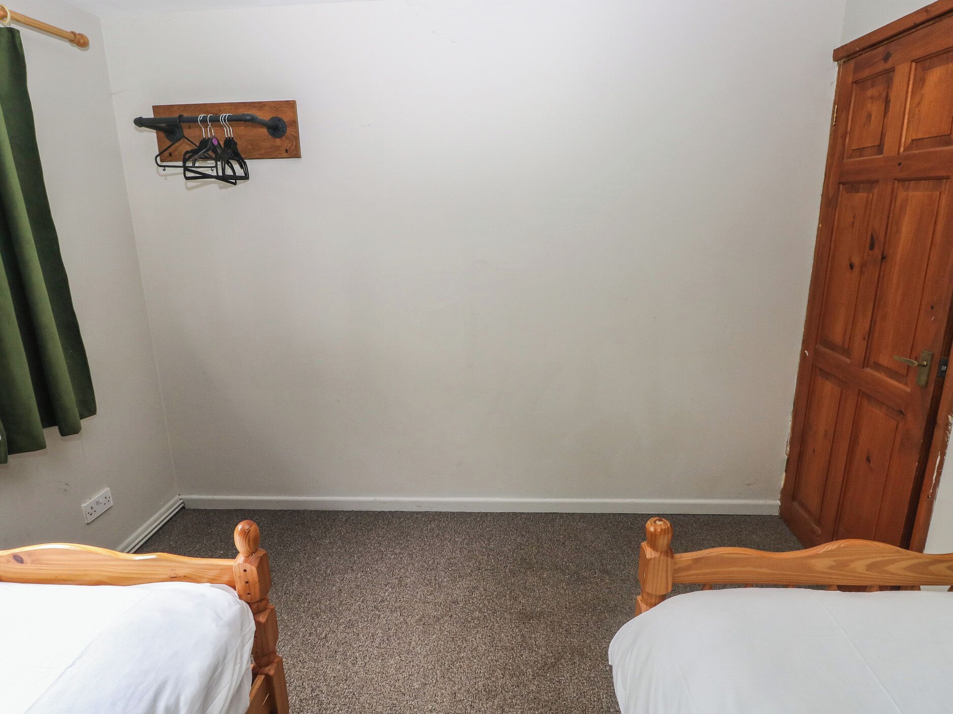 Un dormitorio con dos camas de madera, un armario de madera, un perchero en la pared y una cortina verde.