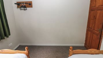 Un dormitorio con dos camas de madera, un armario de madera, un perchero en la pared y una cortina verde.
