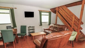 Una sala de estar con un sofá, sillas, una mesita, un televisor y una escalera.
