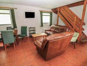 A living room with a sofa, chairs, a small table, a TV, and a staircase. - Cabin No. 13 - Salt and Fern Cabins (Port Talbot)