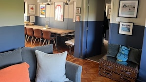Une pièce comprenant une table à manger en bois, des chaises, un canapé, une valise et des tableaux encadrés accrochés aux murs.