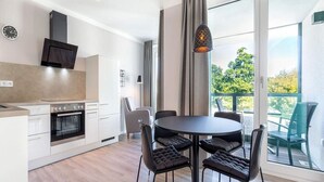 Cozinha moderna com forno embutido, área de refeições com mesa redonda e quatro cadeiras, e uma janela grande com vista para vegetação.