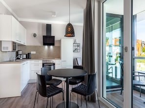 A modern kitchen with white cabinets, a black stove, and a dining area with a round table and four chairs. - 4 Star Holiday Home in Travemunde (Lübeck)