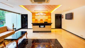 A hotel reception area with a reception desk, a sofa, a coffee table, and a television on the wall. - Deluxeimperial Villa Delhi (New Delhi)
