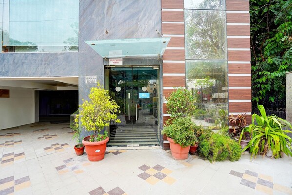 A building entrance with a glass door, potted plants, and a tiled floor.