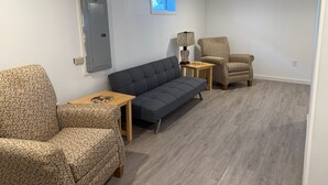 Une pièce avec un canapé gris, un fauteuil à motifs et une petite table en bois sur laquelle se trouve une lampe.