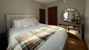 Une chambre à coucher comprenant un lit, une table de chevet en bois, un miroir et un luminaire fixé au plafond.