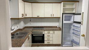A compact kitchen with white cabinets, a built-in oven, a stainless steel sink, and a refrigerator with clear drawers. - Apartment 5 minutes walk from the Fair. Ideal for couples. (Jerez de la Frontera)