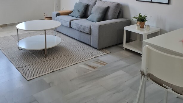 A modern living room with a grey sofa, a round white coffee table, a side table with a plant, and a large mirror on the wall. - Apartment 5 minutes walk from the Fair. Ideal for couples. (Jerez de la Frontera)
