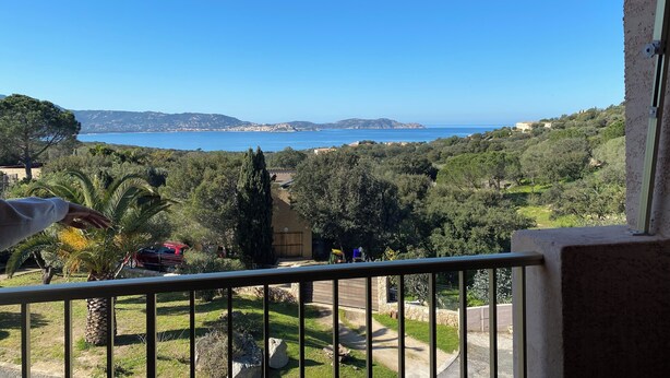 En balkon med udsigt over et kystlandskab, inklusive træer og et fjerntliggende vandområde.