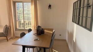 Et spiseområde med et stort bord, stole, en fjernbetjening og et vindue med gardiner.