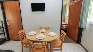 A dining area with a round table, six chairs, and a flat-screen TV mounted on the wall. - Cabin No. 15 - Salt and Fern Cabins (Port Talbot)
