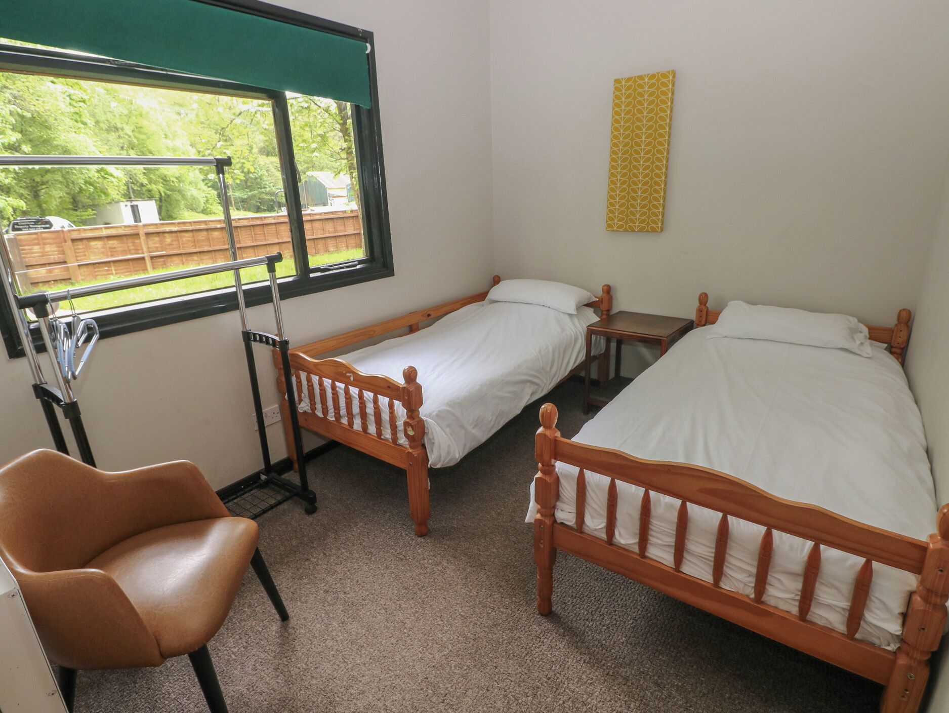 A room with two wooden beds, a chair, a window with a view of a backyard, and a small table.
