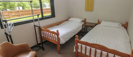 A room with two wooden beds, a chair, a window with a view of a backyard, and a small table.