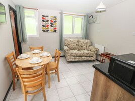 Un espacio habitable compacto con una mesa de comedor preparada para cuatro personas, un sofá estampado, una mesita auxiliar y una zona de kitchenette.