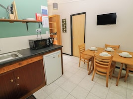 Cocina compacta con microondas, pileta y un refrigerador pequeño. Cuenta con una mesa de comedor con sillas y un televisor montado en la pared.