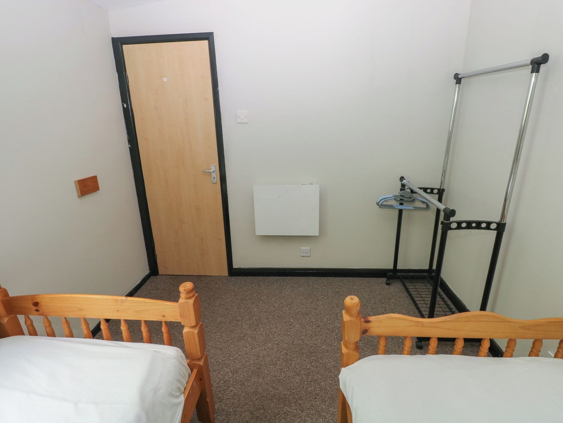 Ein Zimmer mit zwei Holzbetten, einer Tür, einem Heizkörper und einem Geländer.