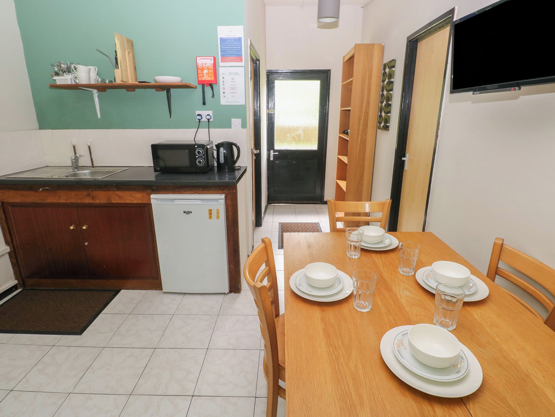 Eine kompakte Küche mit Mikrowelle, Spüle und kleinem Kühlschrank. Ein Esstisch ist mit Tellern und Gläsern gedeckt.