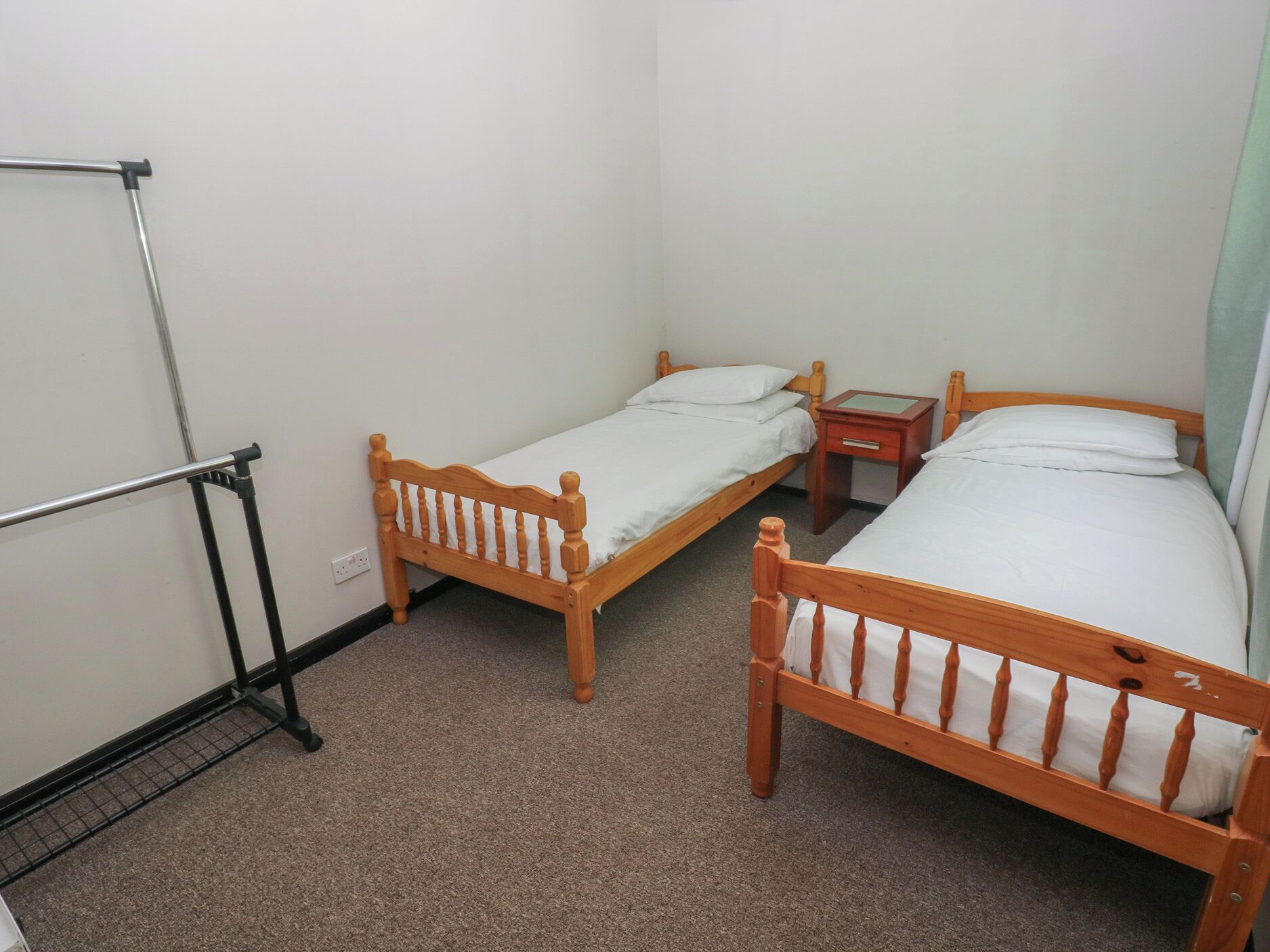 Ein kleines Zimmer mit zwei Holzbetten, einem Metallgestell und einem kleinen Nachttisch aus Holz.